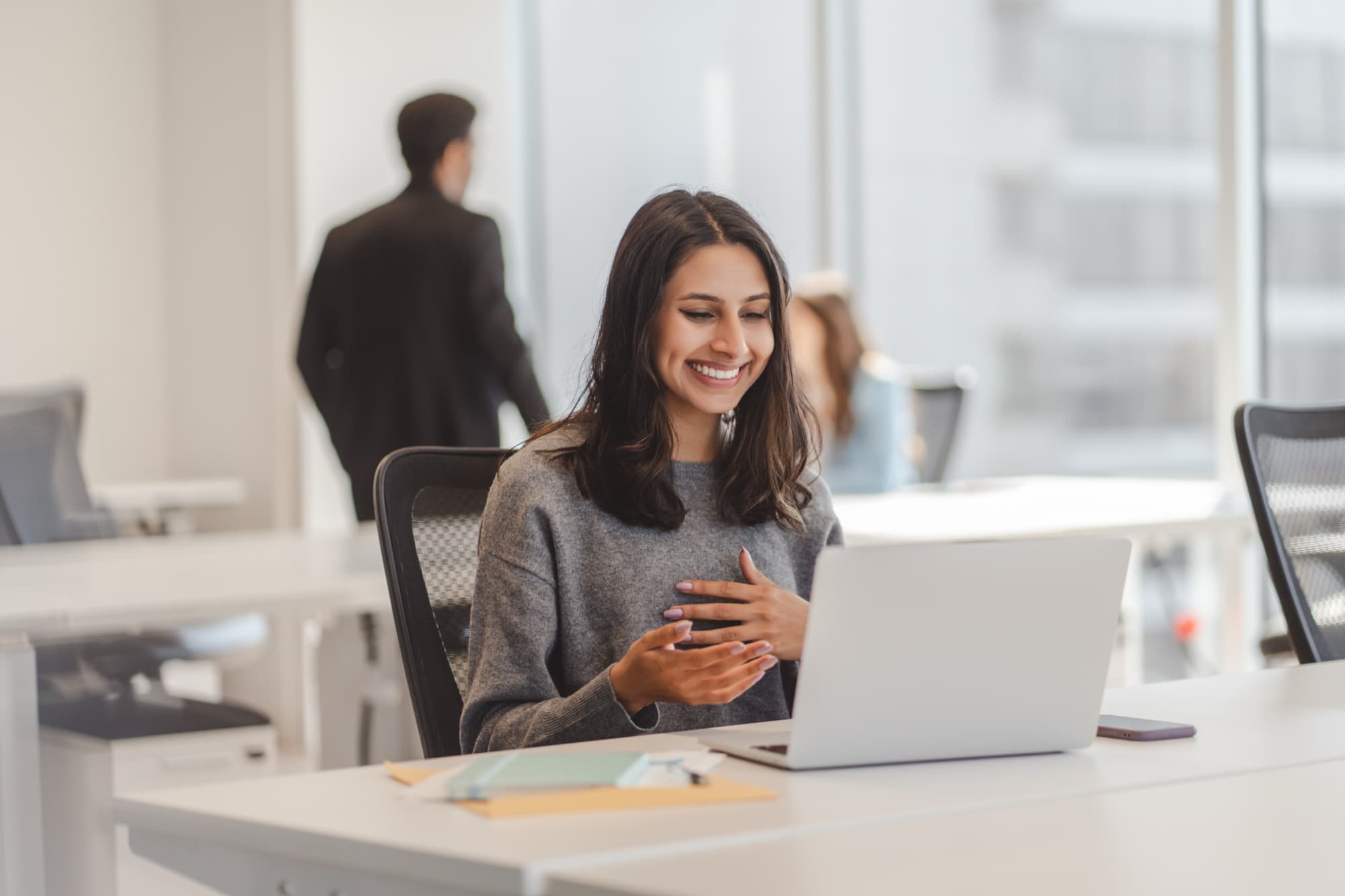 Person smiling at a laptop in a bright office